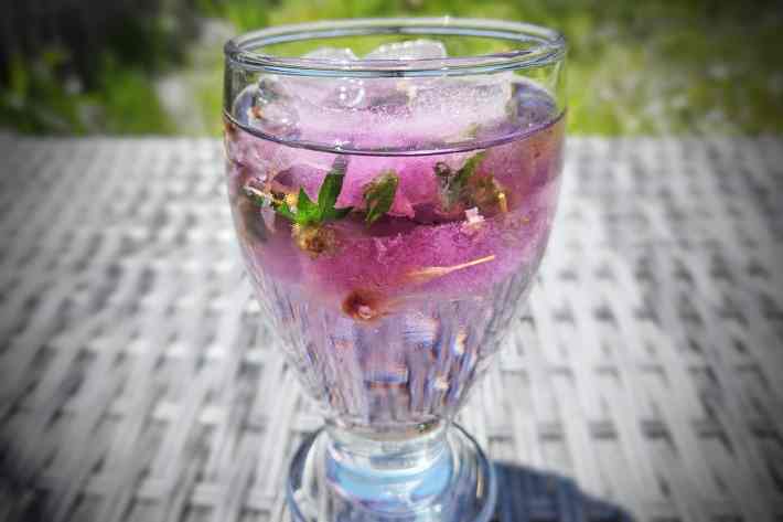 A closeup photograph of a glass full of beautiful, floral herbal ice cubes.