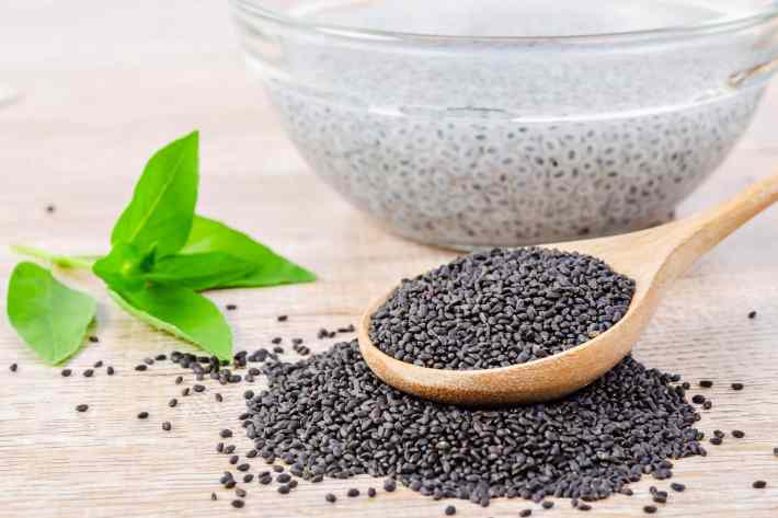 A closeup photograph of a wooden spoon full of sweet basil seeds.